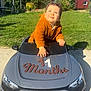 baby, child, toy_car, audi, outdoor, grass, sunny, hoodie, blue_eyes, curly_hair, months, celebration, greenery, daylight, playful, portrait, vehicle, cute, smiling, garden