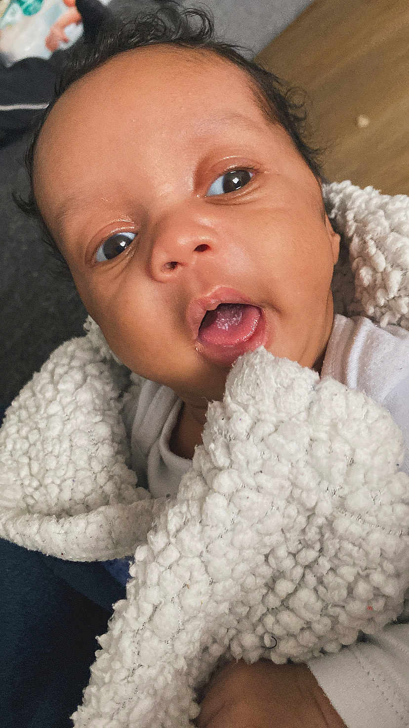 Liam joined the competition — help win amazing prizes! baby, infant, face, blanket, closeup, cute, child, expression, skin, mouth, eyes, curly_hair, white_clothing, soft_texture, indoors, portrait, newborn, young_child, wrapped, cozy