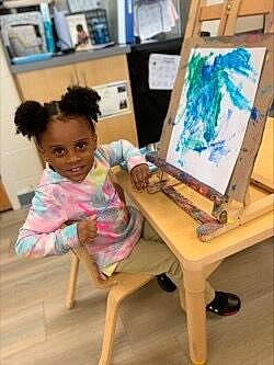 Alannah is registered to the contest to win money with this photo: art, artist, chair, child, design, desk, easel, flooring, fun, furniture, illustration, joy, leisure, paint, painting, person, picture_frame, sitting, table, toddler