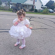 Laykyn is registered to the contest to win money with this photo: child, toddler, girl, portrait, outdoor, street, dress, white_dress, pink_shoes, curly_hair, hair_bows, necklace, bracelet, standing, residential_area, house, road, parked_car, utility_vehicle, trees