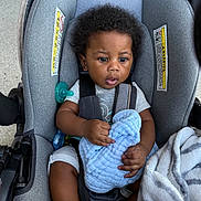 Akyrie is registered to the contest to win money with this photo: baby, car_seat, child, infant, blanket, pacifier, clothing, seatbelt, person, indoors, cute, curly_hair, toddler, soft_texture, gray, blue, comfort, expression, hands, foot