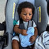 baby, car_seat, child, infant, blanket, pacifier, clothing, seatbelt, person, indoors, cute, curly_hair, toddler, soft_texture, gray, blue, comfort, expression, hands, foot