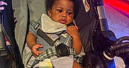 Akyrie joined the competition — help win amazing prizes! baby, baby_bib, black_hair, child, clothing, comfort, curly_hair, cute, diaper, expression, face, hand, indoor, infant, lighting, person, photography, seat, seatbelt, stroller