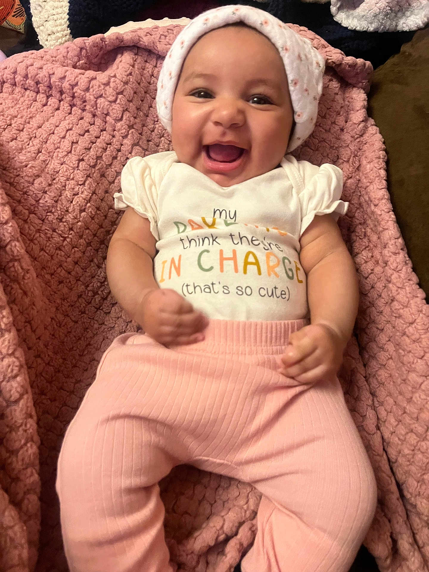 Nova is registered to the contest to win money with this photo: baby, smiling, infant, pink_pants, white_shirt, hat, blanket, happy, cute, lying_down, face, child, young_child, texture, soft, indoors, person, apparel, headwear, portrait