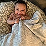 Nova is registered to the contest to win money with this photo: baby, blanket, cushion, smiling, happy, child, infant, texture, pattern, cozy, indoors, cute, person, clothing, face, head, hands, resting, comfort, soft