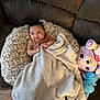 baby, blanket, couch, plush_toy, pillow, smile, infant, cozy, patterned, furniture, child, soft, cute, indoors, relaxing, happy, person, toy, comfort, small