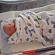 James joined the competition — help win amazing prizes! newborn, baby, hospital, bassinet, blanket, footprint_pattern, hat, sleeping, infant, swaddled, bed, person, child, cute, healthcare, resting, soft, cozy, wrapped, peaceful
