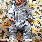 Jermoni is registered to the contest to win money with this photo: baby, child, hoodie, blue_clothing, sneakers, blanket, dinosaur_pattern, infant, cute, lying_down, indoors, footwear, person, soft_texture, clothing, portrait, young_child, casual_wear, comfortable, resting