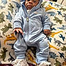 baby, child, hoodie, blue_clothing, sneakers, blanket, dinosaur_pattern, infant, cute, lying_down, indoors, footwear, person, soft_texture, clothing, portrait, young_child, casual_wear, comfortable, resting