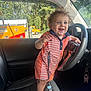 toddler, child, car, steering_wheel, seat, curly_hair, smiling, blue_eyes, orange_truck, window, outdoor, daylight, clothing, pacifier, car_seat, interior, vehicle, happy, person, seat_belt_clip