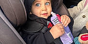 Declan is registered to the contest to win money with this photo: toddler, child, car_seat, hoodie, snack_pouch, blue_eyes, seatbelt, car_interior, plush_toy, clothing, person, seat, window, vehicle, sitting, black_hoodie, blue_pants, hand, face, curious