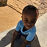 child, boy, outdoor, sidewalk, stone_wall, shadow, blue_shirt, colorful_shoes, sunlight, crouching, concrete, expression, casual_clothing, daylight, young, person, skin, hair, pose, background