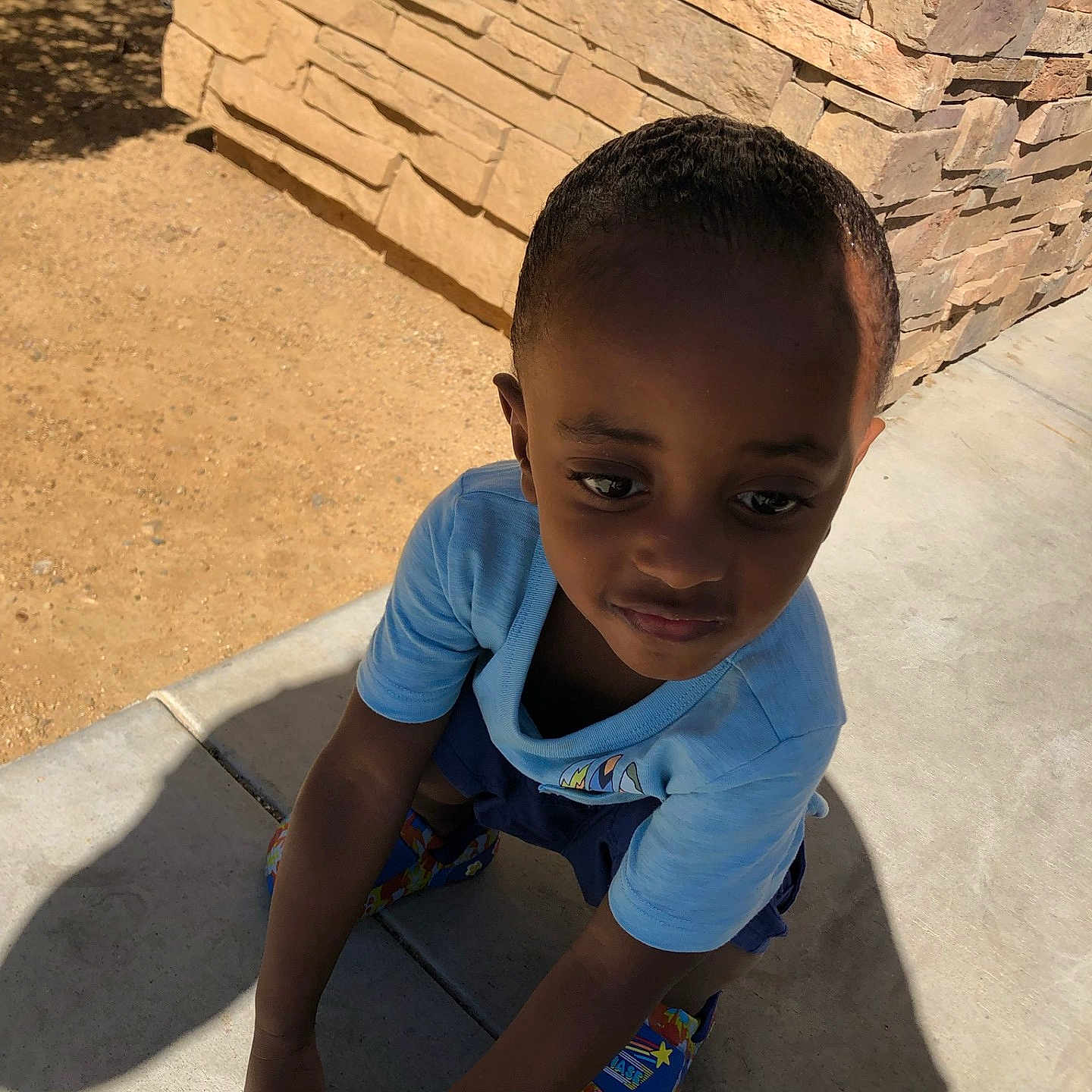 Zaamir Boyd joined the competition — help win amazing prizes! child, boy, outdoor, sidewalk, stone_wall, shadow, blue_shirt, colorful_shoes, sunlight, crouching, concrete, expression, casual_clothing, daylight, young, person, skin, hair, pose, background
