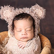 Jahzeiah is registered to the contest to win money with this photo: baby, sleeping, swaddled, knitted_wrap, bear_ears, hat, basket, cozy, peaceful, newborn, infant, cute, portrait, soft_texture, warm_colors, hand, face, closed_eyes, fuzzy, wooden_background