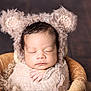 baby, sleeping, swaddled, knitted_wrap, bear_ears, hat, basket, cozy, peaceful, newborn, infant, cute, portrait, soft_texture, warm_colors, hand, face, closed_eyes, fuzzy, wooden_background