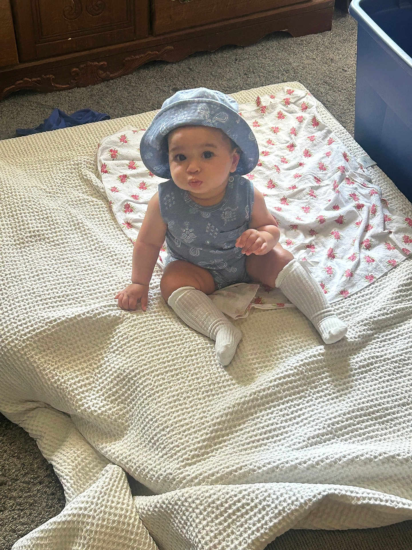 Yamanie is registered to the contest to win money with this photo: baby, bed, blanket, blue_outfit, carpet, child, cute, decor, floor, furniture, hat, home, indoor, person, portrait, pout, sitting, textile, white_socks, young_child