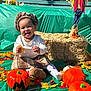 child, toddler, smiling, pumpkin, fall, autumn, leaves, hay_bale, sunflower, outdoor, festive, costume, plaid_skirt, headwear, playful, seasonal, decoration, happy, sitting, toy