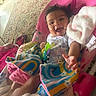 baby, smiling, infant, blanket, colorful, toy, indoor, happy, child, seat, curly_hair, patterned_clothing, carpet, home, reaching_hand, cozy, playful, cute, toddler, baby_bouncer