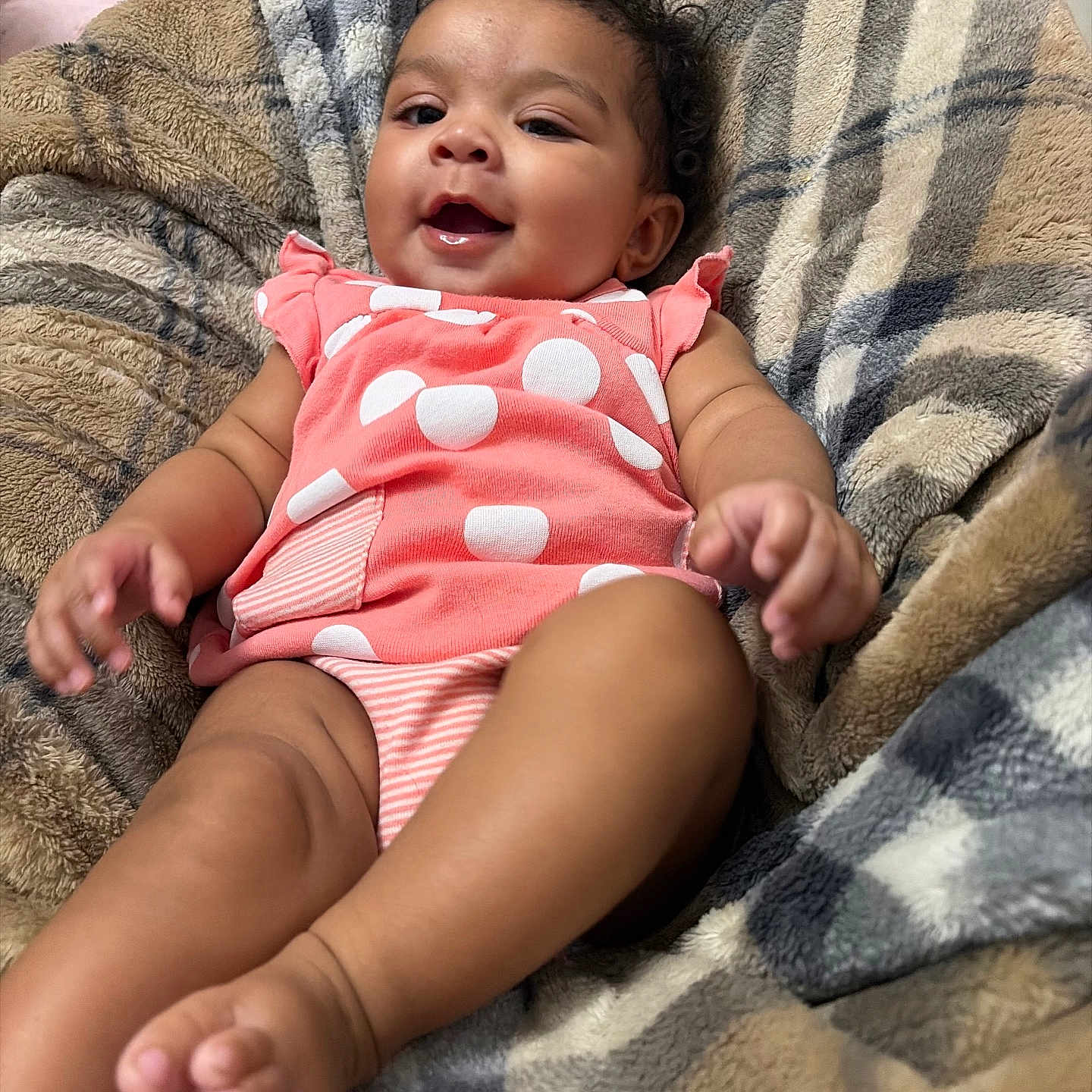 Delilah is registered to the contest to win money with this photo: baby, infant, smiling, pink_clothing, polka_dot, blanket, plaid, cozy, cute, child, happy, indoors, soft_texture, skin, face, hands, feet, curly_hair, relaxed, portrait