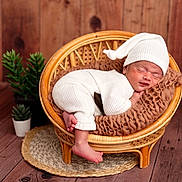 Ethan joined the competition — help win amazing prizes! newborn, baby, sleeping, white_clothing, hat, rattan_chair, brown_cushion, wooden_floor, wooden_wall, potted_plants, cozy, infant, cute, resting, portrait, indoors, soft_texture, small_feet, peaceful, child