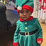 Grace-Edah a rejoint le concours — aidez-le/la à gagner de superbes lots ! toddler, child, elf_costume, green_dress, red_trim, holiday, christmas_tree, indoor, curious_expression, hat, socks, wooden_floor, sofa, curtains, earrings, television, festive, holiday_decor, person, portrait