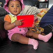 Grace-Edah a rejoint le concours — aidez-le/la à gagner de superbes lots ! toddler, child, pink_hat, pink_socks, red_tablet, bracelet, couch, living_room, indoor, curious, clothing, person, furniture, technology, baby, earrings, sitting, portrait, black_leather, home