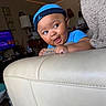 baby, child, infant, portrait, smiling, happy, blue_cap, blue_shirt, face, eyes, indoors, living_room, couch, furniture, home, string_lights, television, blanket, looking_sideways, playful