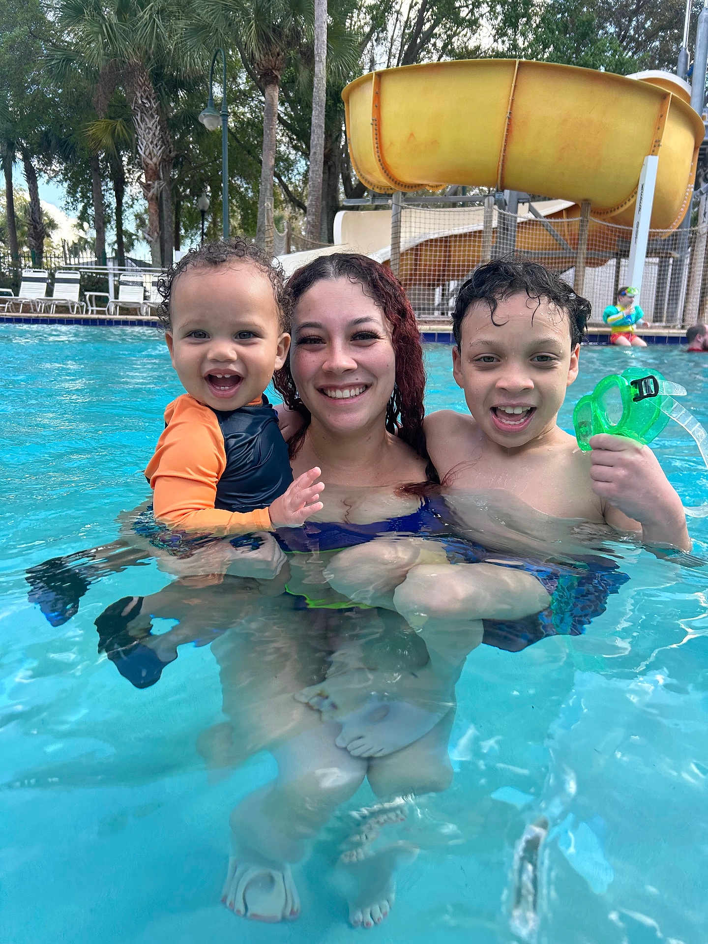 Makenai joined the competition — help win amazing prizes! child, toddler, woman, pool, water_slide, swimming_pool, water, smiling, family, goggles, swimwear, swimsuit, outdoors, palm_trees, reflection, wet_hair, vacation, playful, laughter, lounge_chairs