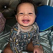 Makenai is registered to the contest to win money with this photo: baby, baby_girl, bed, blanket, child, clothing, curly_hair, cute, face, hands, happy, indoor, infant, onesie, person, pillow, portrait, sitting, skin, smile