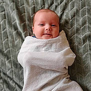 Jett is registered to the contest to win money with this photo: baby, blanket, wrapped, smiling, face, infant, texture, gray, soft, cozy, child, cute, portrait, lying_down, warm, comfort, newborn, young_child, indoors, peaceful