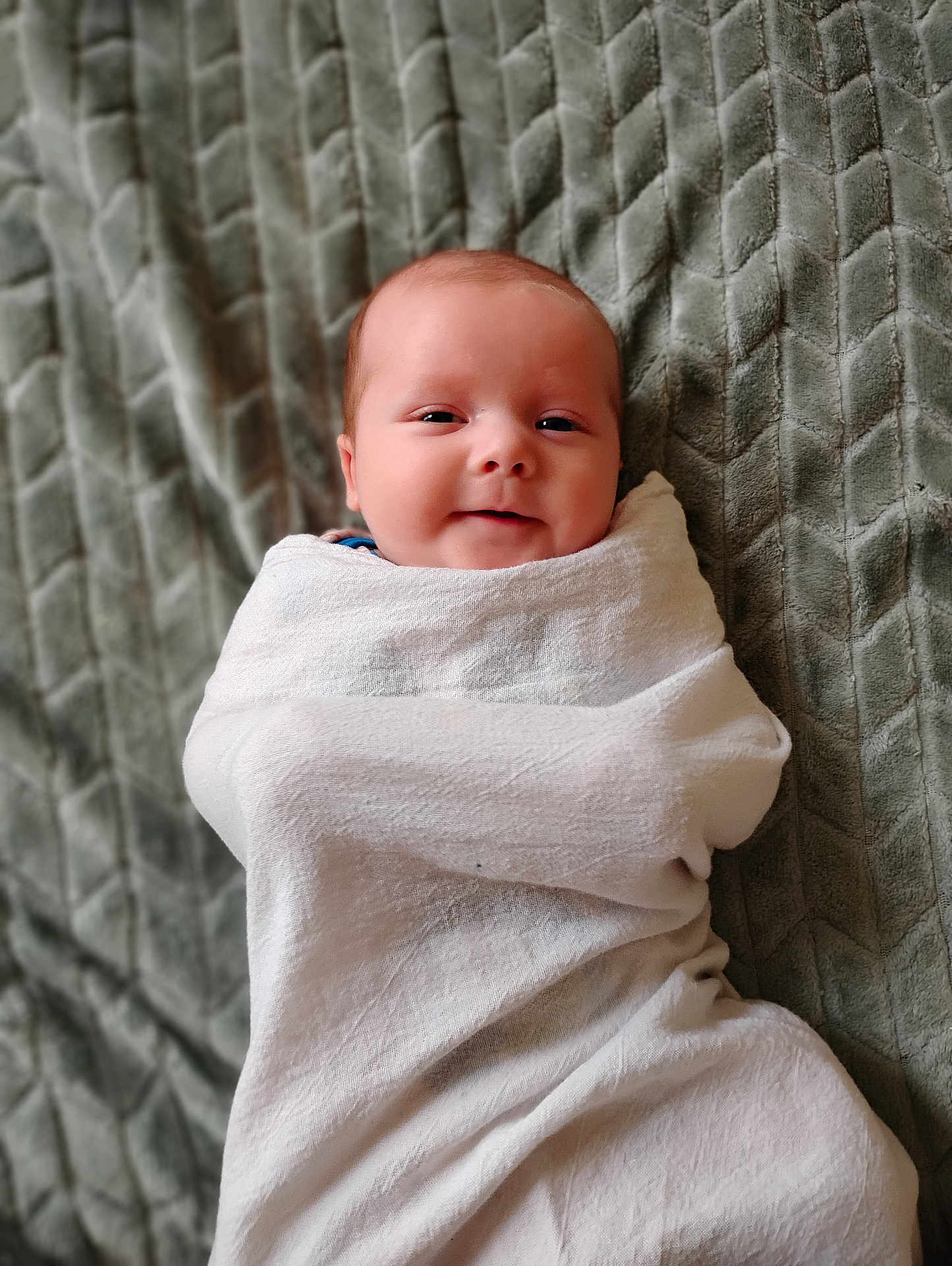 Jett is registered to the contest to win money with this photo: baby, blanket, wrapped, smiling, face, infant, texture, gray, soft, cozy, child, cute, portrait, lying_down, warm, comfort, newborn, young_child, indoors, peaceful