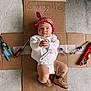 baby, infant, diaper, bandana, face_paint, tools, cardboard, boots, floor, concrete, red_bandana, white_shirt, screwdriver, pliers, level_tool, curious_expression, child, indoors, hand_clasped, young_baby