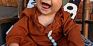 Kohen is registered to the contest to win money with this photo: baby, child, smiling, laughing, hat, pacifier, beads, cushion, rocking_chair, wood, outdoor, brick_wall, pillow, clothing, footwear, cute, happy, infant, portrait, seat