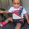 baby, black_skin, casual_clothing, chair, child, concrete_floor, curly_hair, expression, feet, legs, office_chair, outdoor, person, portrait, red_socks, shorts, sitting, toddler, tshirt, young_child