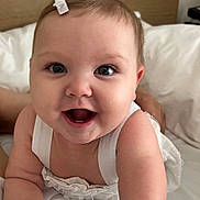 Juliet Marie Willey is registered to the contest to win money with this photo: baby, child, smiling, white_clothing, hair_clip, bed, pale_skin, happy, portrait, cute, infant, closeup, hands, face, eyes, indoor, soft_light, young_child, person, baby_girl