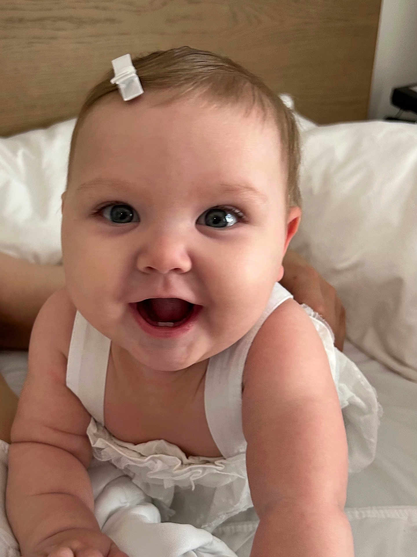 Juliet Marie Willey is registered to the contest to win money with this photo: baby, child, smiling, white_clothing, hair_clip, bed, pale_skin, happy, portrait, cute, infant, closeup, hands, face, eyes, indoor, soft_light, young_child, person, baby_girl