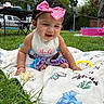 Kayani joined the competition — help win amazing prizes! baby, child, bow, curly_hair, blanket, grass, outdoor, picnic_table, person, smiling, crawling, headband, clothing, earrings, toy, adult, greenery, fence, daylight, playtime