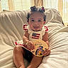 Kayani is registered to the contest to win money with this photo: baby, child, curly_hair, smiling, tongue_out, sitting, blanket, plush, indoor, window, curtains, sunlight, celebration, 4th_of_july, american_flag, dress, hair_accessories, cute, happy, portrait