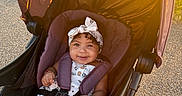 Kayani joined the competition — help win amazing prizes! baby, stroller, child, outdoor, sunlight, smile, headband, curly_hair, seatbelt, toy, happy, daylight, path, infant, cute, summer, playful, sitting, person, accessory
