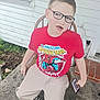 child, boy, glasses, red_shirt, spiderman, t_shirt, sitting, porch, chair, smartphone, concrete, house_siding, statue, missing_tooth, sneakers, casual_clothing, window, outdoor, smile, young_person
