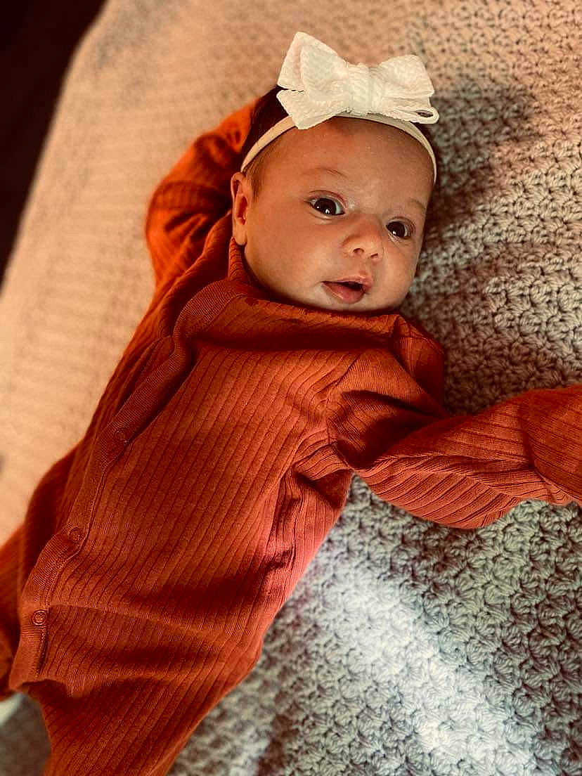 Kailani is registered to the contest to win money with this photo: baby, baby_toddler_clothing, cheek, comfort, eye, face, fashion_accessory, flooring, fur, headband, headgear, iris, linens, peach, person, sitting, sleeve, textile, toddler, wood