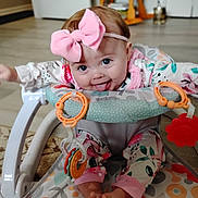 Lainey is registered to the contest to win money with this photo: baby, child, infant, smiling, tongue_out, pink_bow, headband, blue_eyes, sitting, activity_walker, baby_toys, toy_rings, colorful, floral_clothing, patterned_mat, indoor, living_room, portrait, playtime, happy