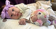 Myla is registered to the contest to win money with this photo: baby, headband, purple, stuffed_animal, toy, blanket, infant, laying_down, soft_toys, cute, indoor, child, portrait, clothing, pink, white, face, hand, closeup, cozy