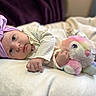 baby, headband, purple, stuffed_animal, toy, blanket, infant, laying_down, soft_toys, cute, indoor, child, portrait, clothing, pink, white, face, hand, closeup, cozy