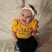 Myla is registered to the contest to win money with this photo: baby, child, smiling, yellow_shirt, headband, sitting, happy, indoor, clothing, person, portrait, cute, infant, face, young_child, white_socks, black_pants, soft_background, casual, playful