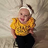 baby, child, smiling, yellow_shirt, headband, sitting, happy, indoor, clothing, person, portrait, cute, infant, face, young_child, white_socks, black_pants, soft_background, casual, playful