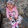 Myla is registered to the contest to win money with this photo: baby, child, smile, pink_clothing, headwrap, couch, floral_pattern, cow_print, socks, seated, indoors, portrait, cute, happy, person, infant, fashion, patterned_fabric, home, casual