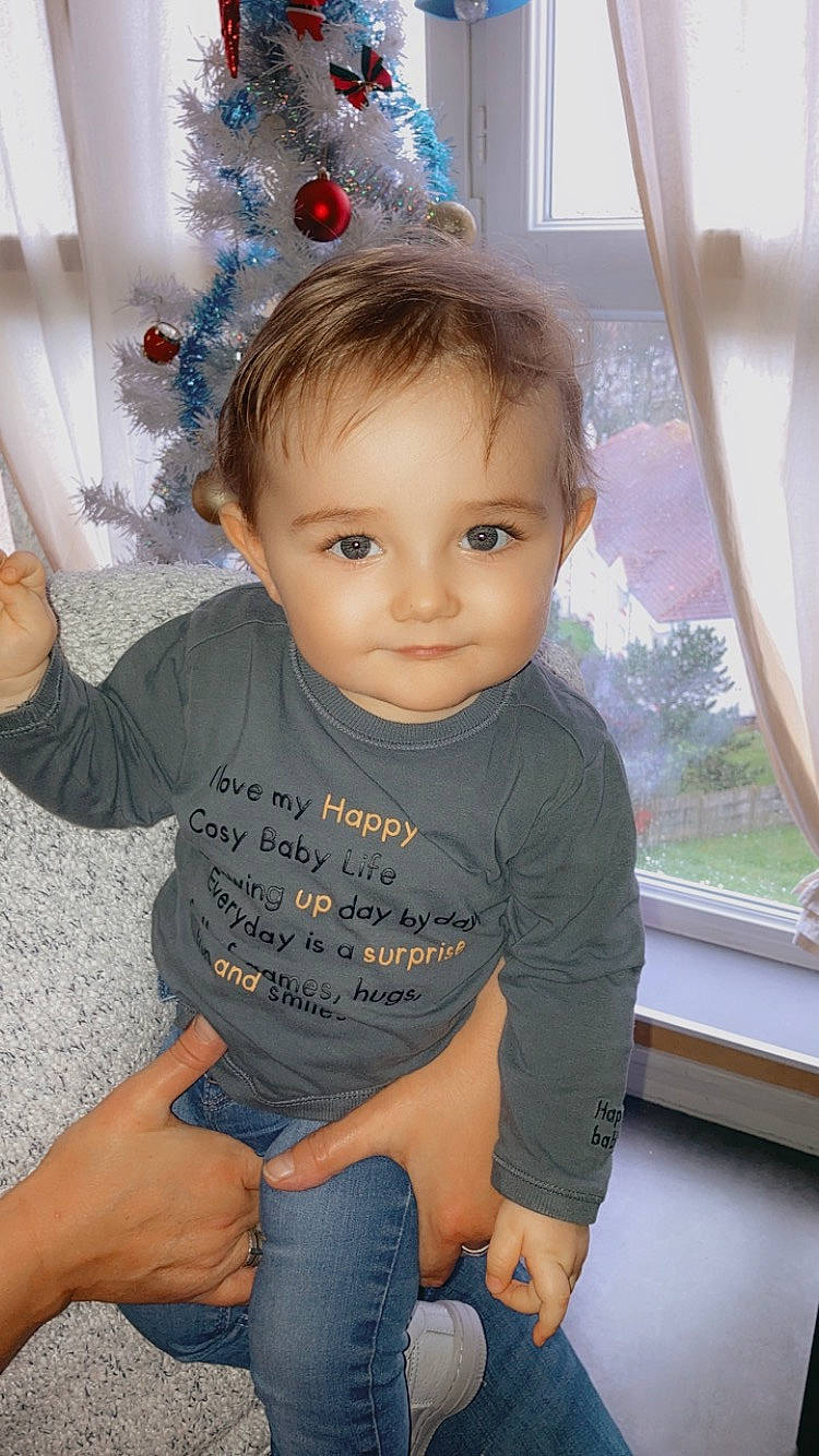 Emiliano a rejoint le concours — aidez-le/la à gagner de superbes lots ! baby_toddler_clothing, blue, cheek, christmas_ornament, facial_expression, fun, hair, hairstyle, happy, head, holiday_ornament, iris, joy, neck, person, skin, sleeve, standing, thigh, toddler