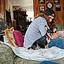 dog, person, couch, blanket, indoor, wooden_wall, family_photos, clock, fan, cat_tree, casual_clothing, cap, striped_shirt, long_hair, curly_hair, pet, seated, relaxed, living_room, home_decor