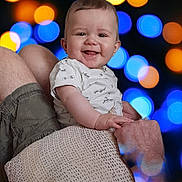 Sasha participe au concours pour gagner de l'argent avec cette photo : baby, child, smile, happy, person, holding, adult, arm, shorts, shirt, pattern, face, skin, head, background, bokeh, lights, colorful, blur, portrait